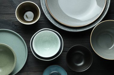 Stylish empty dishware on black wooden table, flat lay