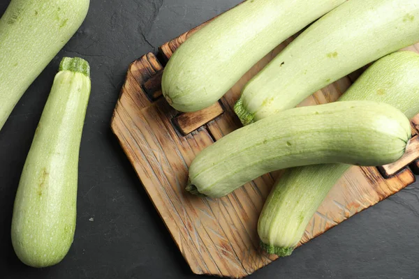 Raw green zucchinis and wooden board on black slate table, flat lay