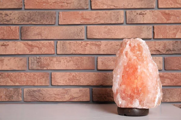 Himalayan salt lamp on table near brick wall. Space for text
