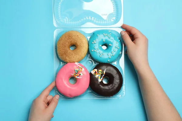 Woman with box of delicious donuts on light blue background, top view