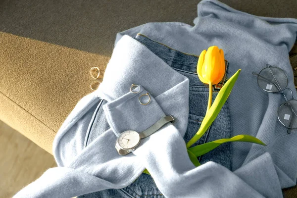 Soft cashmere sweater, jeans, accessories and tulip on sofa