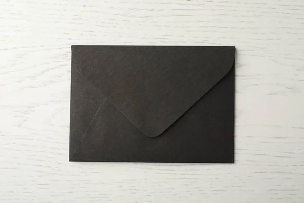 Black paper envelope on white wooden background, top view