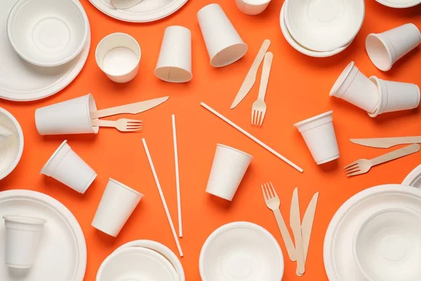 Disposable tableware on orange background, flat lay