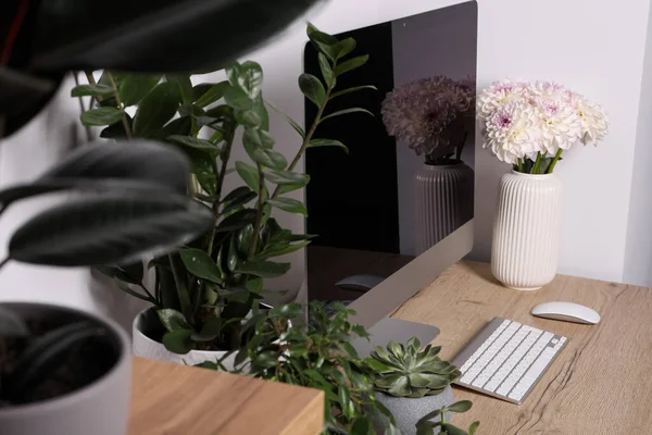 Comfortable workplace with modern computer, green houseplants and beautiful flowers on wooden table indoors