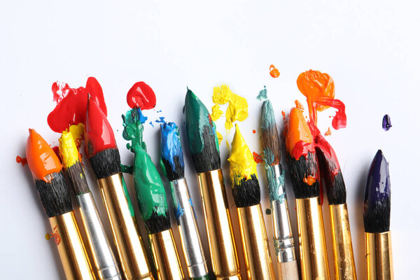 Brushes with colorful paints on white background, closeup