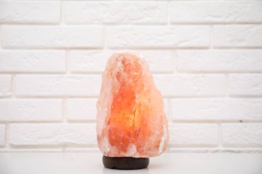 Himalayan salt lamp on table near white brick wall