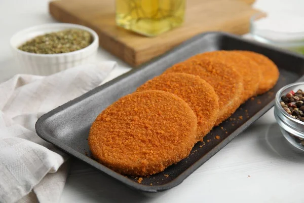 Uncooked breaded cutlets on white wooden table. Freshly frozen semi-finished product