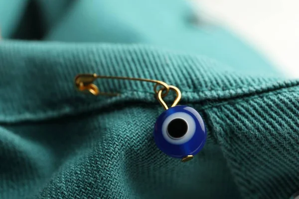 Evil eye safety pin on denim clothing, closeup