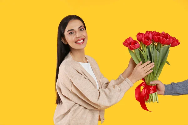 黄色の背景の男から赤いチューリップの花束を受け取った幸せな女性 3月8日 — ストック写真