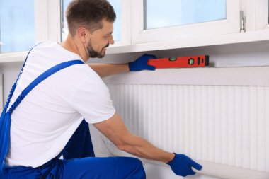 Profesyonel tesisatçı, yeni ısıtma radyatörünü içeri yerleştirmek için balon seviyesini kullanıyor.