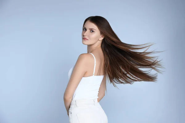 Young woman with strong healthy hair on light blue background