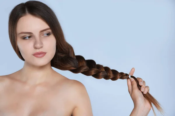 Young woman with strong healthy braided hair on light blue background, space for text