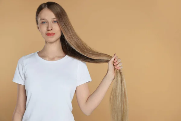 Teenage girl with strong healthy hair on beige background, space for text