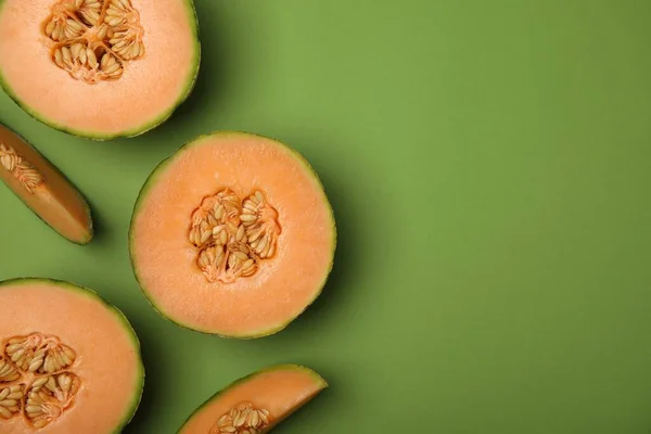 Cut melons on green background, flat lay. Space for text