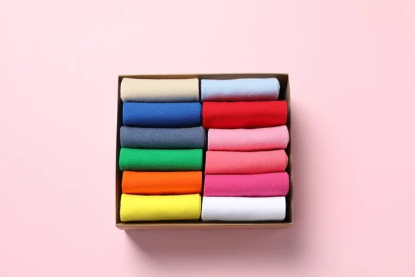 Box with different colorful socks on light pink background, top view