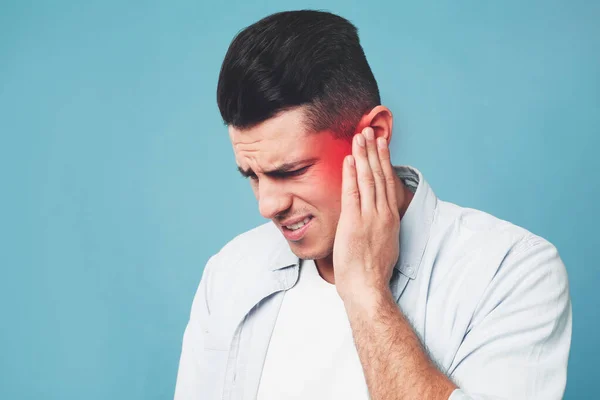 Man suffering from ear pain on light blue background