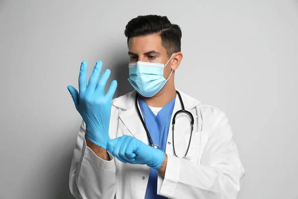 Doctor Beschermende Masker Zetten Medische Handschoenen Tegen Lichtgrijze Achtergrond — Stockfoto