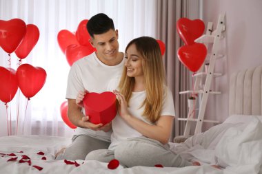 Erkek, kalp şeklinde balonlarla süslenmiş kız arkadaşına hediye sunar. Sevgililer Günü kutlaması