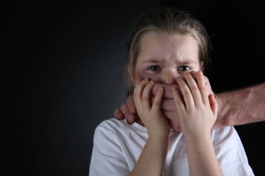 Siyah arka planda korkmuş küçük kızın ağzını kapatan bir adam, mesaj için boşluk. Aile içi şiddet