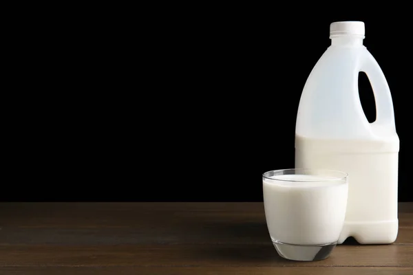 Gallon bottle and glass of milk on wooden table. Space for text