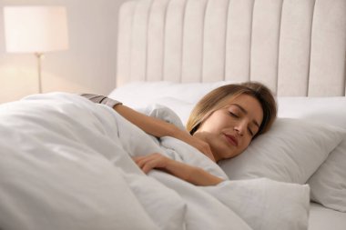 Woman under warm white blanket sleeping in bed indoors