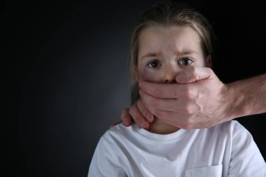 Siyah arka planda korkmuş küçük kızın ağzını kapatan bir adam, mesaj için boşluk. Aile içi şiddet