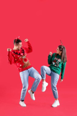 Noel Baba şapkalı ve Noel kazaklı güzel çift kırmızı arka planda eğleniyor.