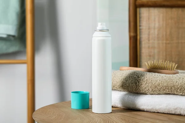 Bottle of dry shampoo, towels and hairbrush on wooden table indoors