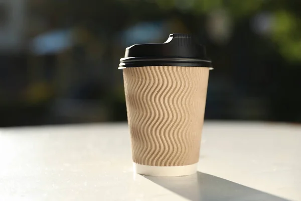 Cardboard takeaway coffee cup with plastic lid on white table outdoors