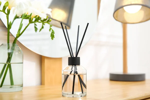 Aromatic reed air freshener and flowers on wooden table in room