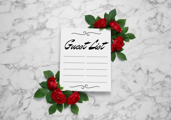 Beautiful flowers and guest list on white marble background, flat lay