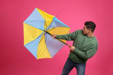 Man with umbrella caught in gust of wind on pink background