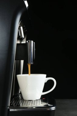 Modern espresso makinesi siyah arka plana karşı gri masaya kahve koyuyor.