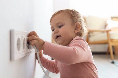 Cute baby playing with electrical socket and plug at home. Dangerous situation