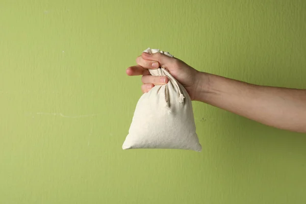 Woman holding full cotton eco bag on light green background, closeup