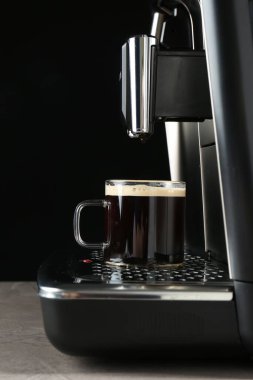 Modern espresso makinesi. Gri masada, siyah arka planda cam kahve fincanı var.