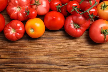 Many different ripe tomatoes on wooden table, flat lay. Space for text