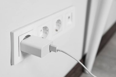 Charger adapter plugged in power socket indoors, closeup. Space for text