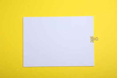 Sheet of paper with clip on yellow background, top view