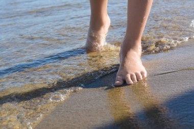 Child walking through water on seashore, closeup of legs
