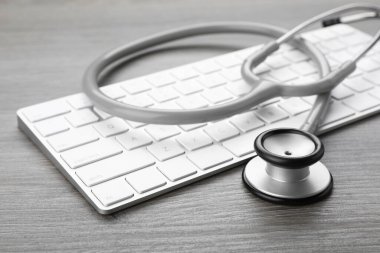 Computer keyboard with stethoscope on wooden table, closeup