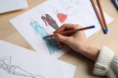 Moda tasarımcısı ahşap masadaki eskiz defterinde yeni kıyafetler yaratıyor.