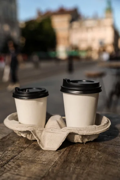 Cardboard takeaway coffee cups with plastic lids and holder on wooden table in city