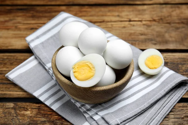 Bowl with hard boiled eggs and kitchen towel on wooden table