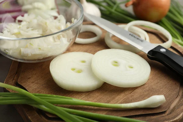 Fresh onion and knife on wooden board, closeup