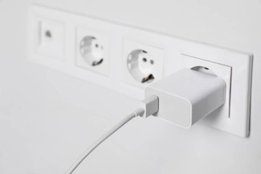 Charger adapter plugged in power socket indoors, closeup. Space for text
