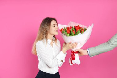 Mutlu kadın pembe arka plandaki adamdan kırmızı lale buketi alıyor. 8 Mart kutlamaları