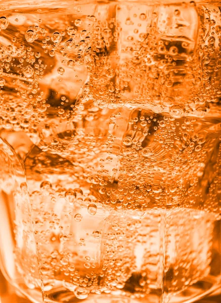 Closeup view of soda water with ice in glass. Toned in glass