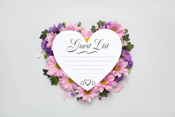 Beautiful flowers and guest list on white background, top view