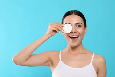 Young woman using cotton pad with micellar water on light blue background